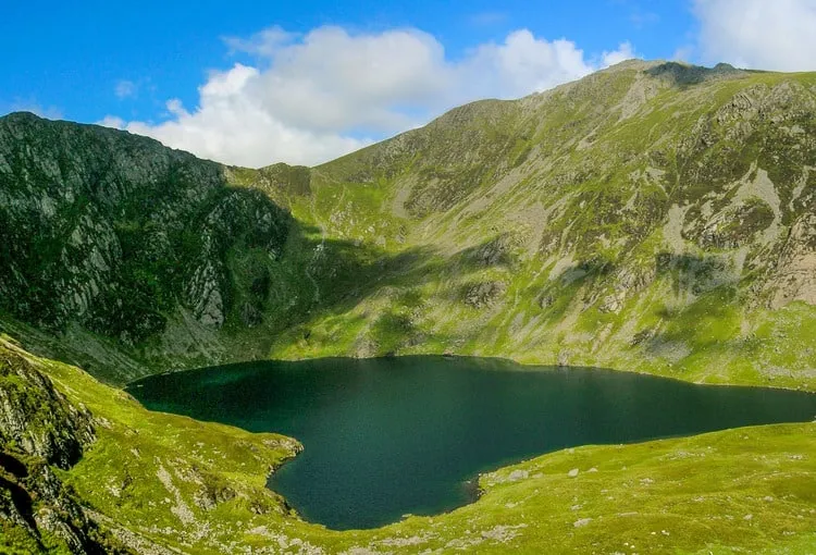 The dark waters of Llyn Cau lake in a steep green and rocky cwm below the summit of Cadair Idris