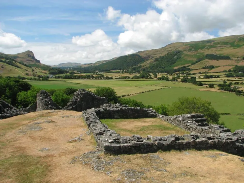 The low stone wall ruins of Castell y Bere on a grassy hilltop, looking out over the green fields and hills of the Dysynni valley